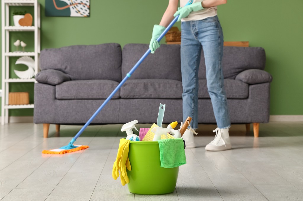 Cleaner mopping a wood floor with a green bucket of supplies in the foreground